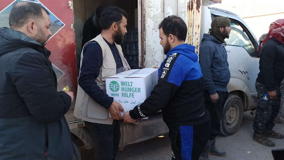 Ein Mann überreicht einem anderen Mann ein Paket mit Hilfsgütern von der Welthungerhilfe