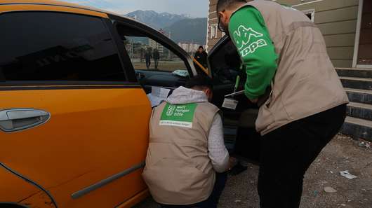 Zwei Welthungerhilfe-Mitarbeiter stehen neben einem Taxi.