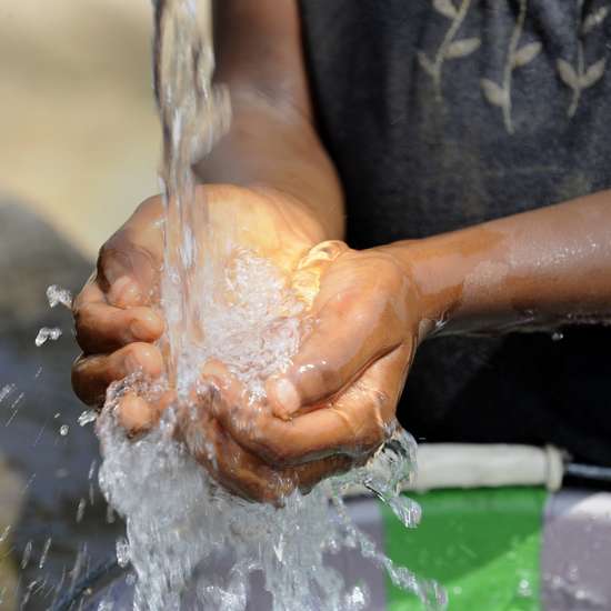 Zugang zu Wasser: Hände schöpfen Wasser unter einem Wasserstrahl.