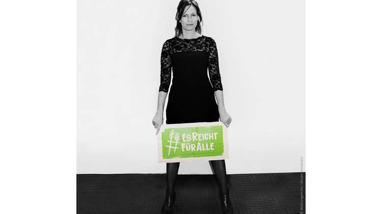 Schauspielerin Nina Kronjäger hält ein Schild mit dem Welthungerhilfe-Hashtag #EsReichtFürAlle.