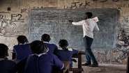 Unterricht in einer Schule im Südsudan: Ein Lehrer steht vor der Tafel, mehrere Kinder sind von hinten zu sehen. 