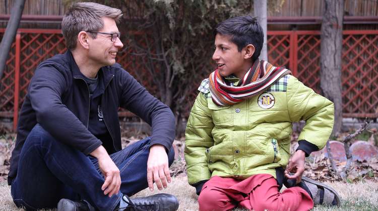 Mathias Mogge sitzt mit einem Jungen auf dem Boden und unterhält sich, Afghanistan 2022.