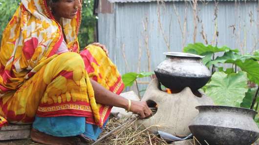 Eine Frau in Bangladesch erhitzt Lebensmittel in einem Topf über dem Feuer.
