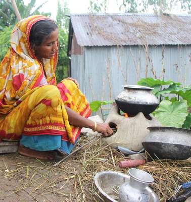Eine Frau in Bangladesch erhitzt Lebensmittel in einem Topf über dem Feuer.