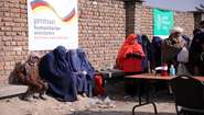Verschleierte Frauen warten bei einer Lebensmittelverteilung. Im Hintergrund sind Banner mit Welthungerhilfe-Logo und von German Humanitarian Assisstance zu sehen.
