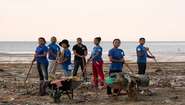 Ein Team aus sieben Personen mit Schubkarren und Schaufeln beseitigt Müll an einem Strand.
