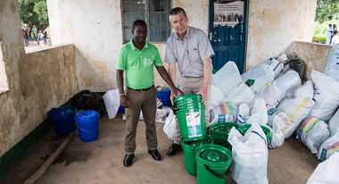 Zwei Männer, einer davon trägt ein grünes Welthungerhilfe-T-Shitrt, stehen vor großen Säcken voller Hilfsgüter.