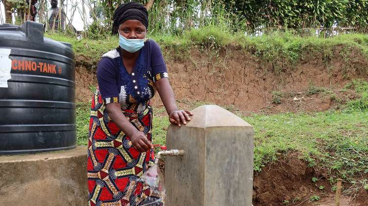 Eine Frau steht an einer Wasserpumpe, Kongo 2021.