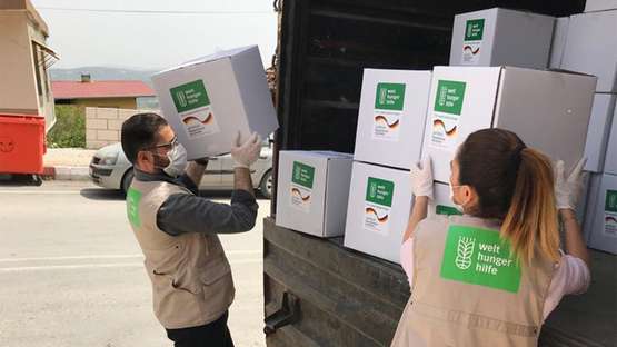 Zwei Welthungerhilfe-Mitarbeiter*innen nehmen Pakete mit Welthungerhilfe-Logo aus einem Lastwagen.