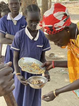 Mädchen stehen mit Tellern in einer Reihe, Südsudan 2022.