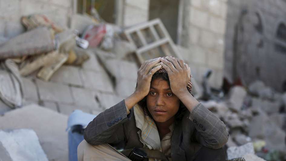 Ein junger Mann sitzt auf einem Trümmerhaufen und stützt den Kopf in die Hände. Sein Blick ist verzweifelt.