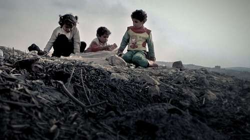 Kinder sitzen auf einem Trümmerhaufen.