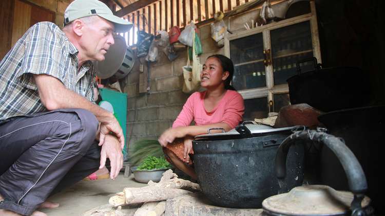 Ein Mann hockt neben einer Frau in einem Haus in Laos.