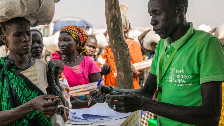 Nothilfe im Südsudan: Eine Frau in traditioneller Kleidung und ein Mann mit grünem Welthungerhilfe T-Shirt bei der Übergabe von Registrierungskarten.