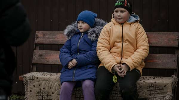 Zwei ukrainische Kinder aus einem Dorf in der Region Charkiw sitzen auf einer Bank