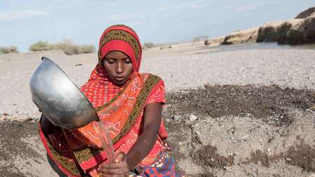Eine Frau füllt in der Wüste Wasser aus einer Schüssel in einen Wasserkanister.
