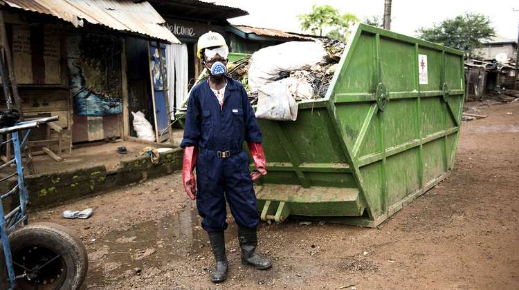 Arbeiter in Schutzkleidung vor einem mit Müll gefüllten Container