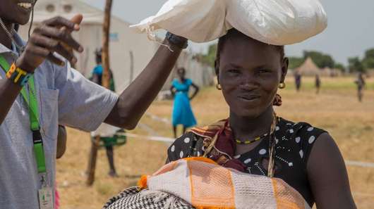 Ein Welthungerhilfe-Mitarbeiter überreicht einer Frau mit Baby im Arm ein Lebensmittelpaket.