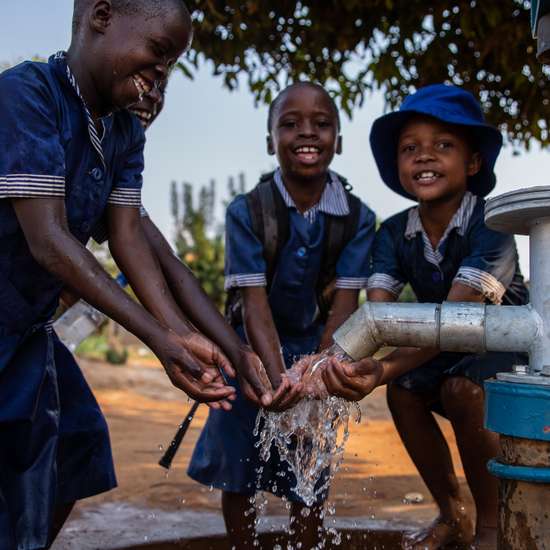 Kinder waschen sich an einem Brunnen die Hände.