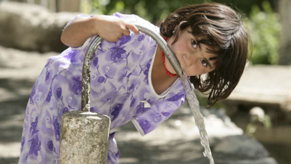 Ein Kind in Tadschikistan trinkt aus einem Brunnen.