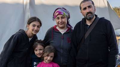 Erdbeben in der Türkei: Eine Familie steht vor einem Zelt, sie alle schauen in die Kamera.