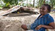 blinde Frau sitzt vor zerstörtem Haus