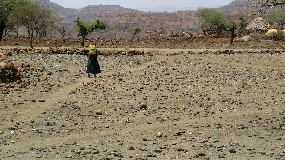 Ein Kind holt Wasser mit einem Kanister und geht durch eine ausgetrocknete Landschaft.