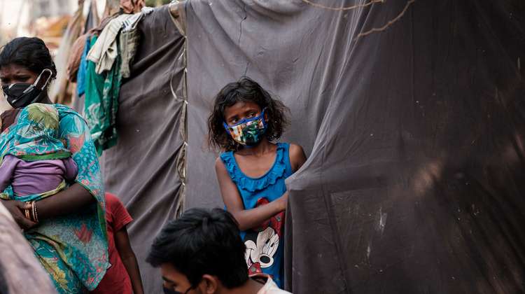 Ein Mädchen mit Mundschutz steht an einem Zelt aus schwarzen Planen.
