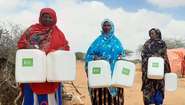 Drei Frauen stehen nebeneinander, sie halten alle zwei Wasserbehälter mit Welthungerhilfe-Logo.