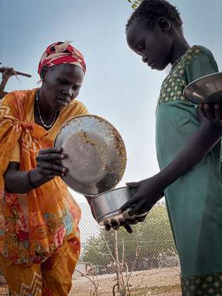Eine Frau verteilt Essen an ein Schulkind in Rubkona, Südsudan.