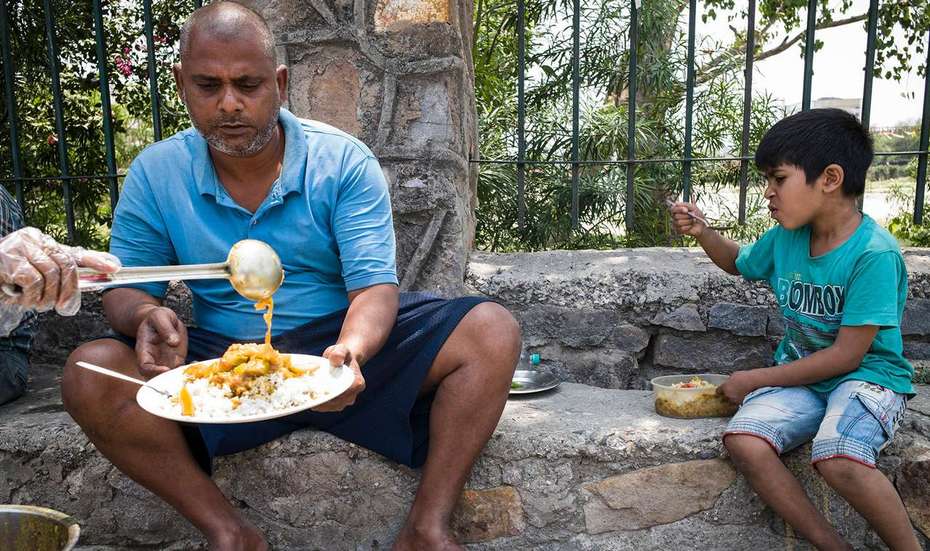 Ein Mann und ein Junge sitzen nebeneinander auf einer Stufe und bekommen Essen auf einen Teller geschöpft.