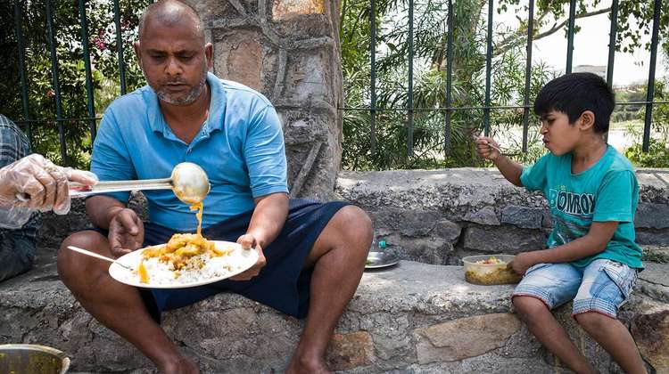 Ein Mann und ein Junge sitzen nebeneinander auf einer Stufe und bekommen Essen auf einen Teller geschöpft.