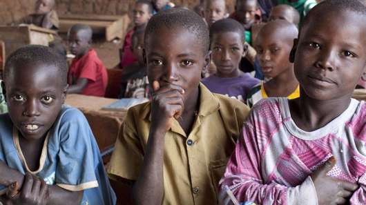 Drei Jungen sitzen im Vordergrund einer Schulklasse in Burundi