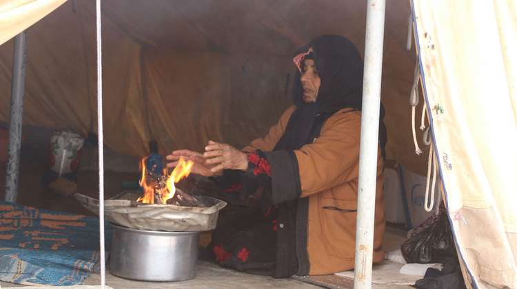 Eine Frau sitzt in einem Zelt und wärmt sich ihre Hände an einem Feuer.