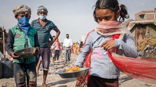 Coronavirus in Indien: Zwei Kinder und ein Mann mit Masken oder Tücher um den Mund bei der Essensausgabe in einem Slum in Indien.
