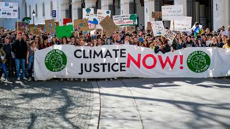 Menschen demonstrieren und halten ein Banner mit der Aufschrift "Climate Justice Now"
