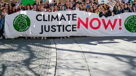 Menschen demonstrieren und halten ein Banner mit der Aufschrift "Climate Justice Now"