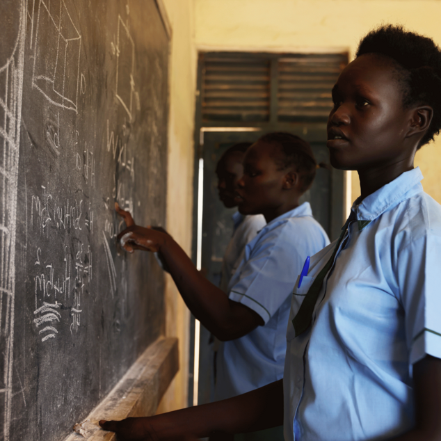 Bild aus einem Projekt im Südsudan mit Schulspeisungen, ein Mädchen steht an einer Schultafel.
