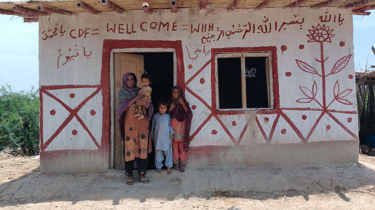 Eine Familie steht in der Tür eines von Hand bemalten kleinen Hauses.
