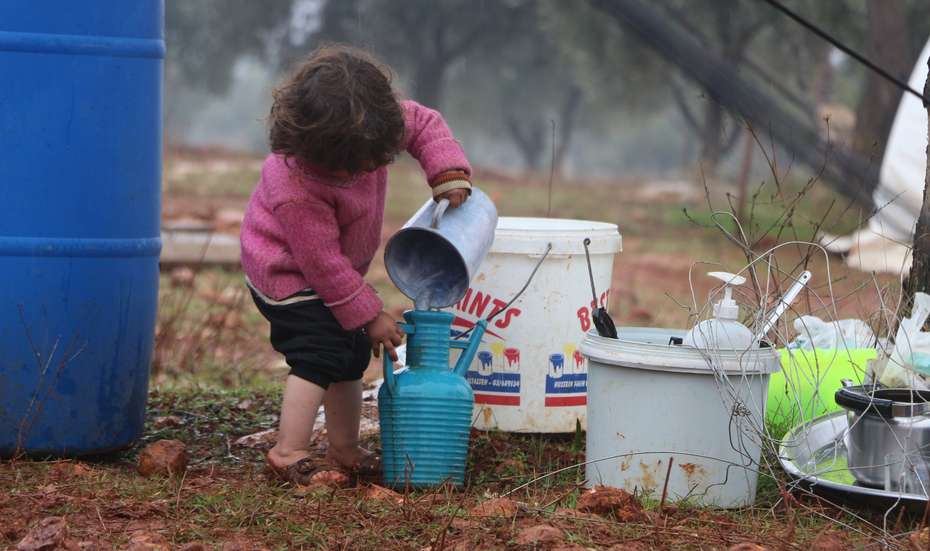 Ein kleines Kind gießt Wasser in einen Krug.