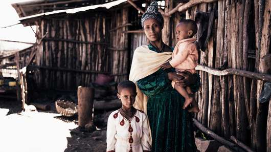Eine Frau steht mit ihren beiden Kindern vor einer Holzhütte, Äthiopien.
