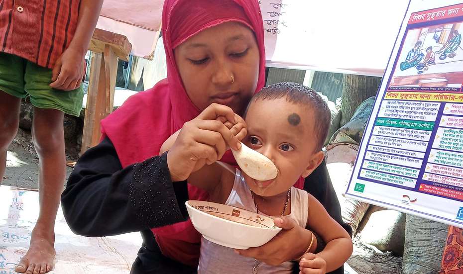 Eine Frau füttert ein Kleinkind, das auf ihrem Schoß sitzt.