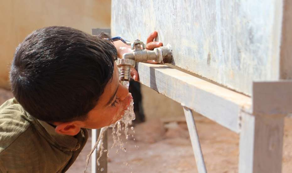 Ein Junge trinkt an einem Wasserhahn.