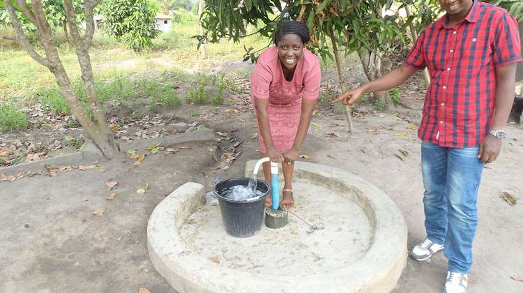 Eine Frau und ein Mann stehen an einer Wasserpumpe, Sierra Leone 2021.