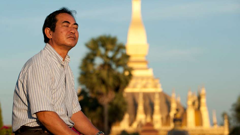 Ein Mann sitzt vor einem Tempel in Laos.