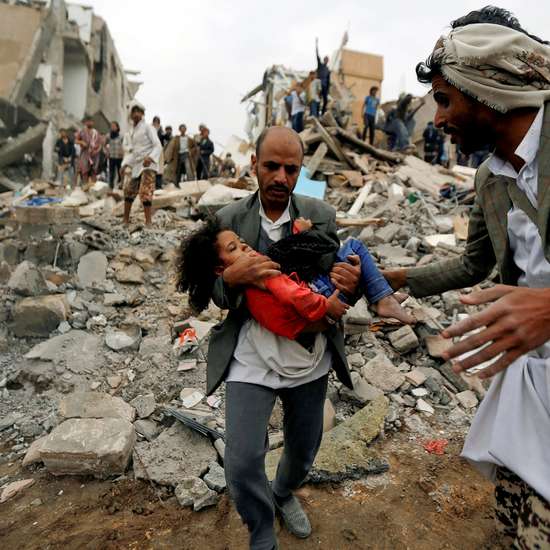 Ein Mann trägt ein Mädchen durch Trümmer im Jemen.