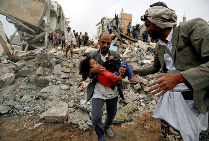 Ein Mann trägt ein Mädchen durch Trümmer im Jemen. 