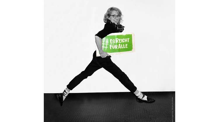 Schauspielerin Anna Böttcher hält ein Schild mit dem Welthungerhilfe-Hashtag #EsReichtFürAlle.
