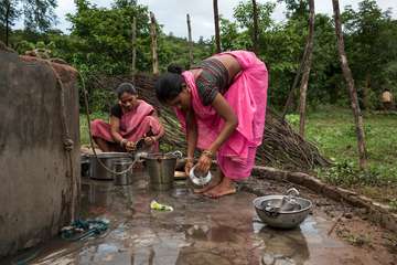 Zwei Frauen waschen in einem Brunnen in indien gemeinsam Geschirr.