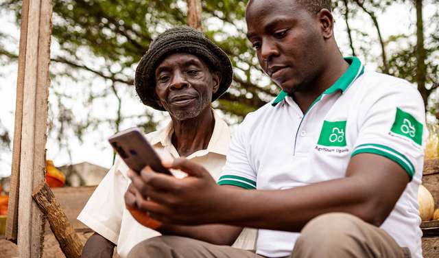 Zwei Kleinbauern schauen in ihr Smartphone und beschäftigen sich mit der Landwirtschafts-App AgriShare, Uganda 2021.
